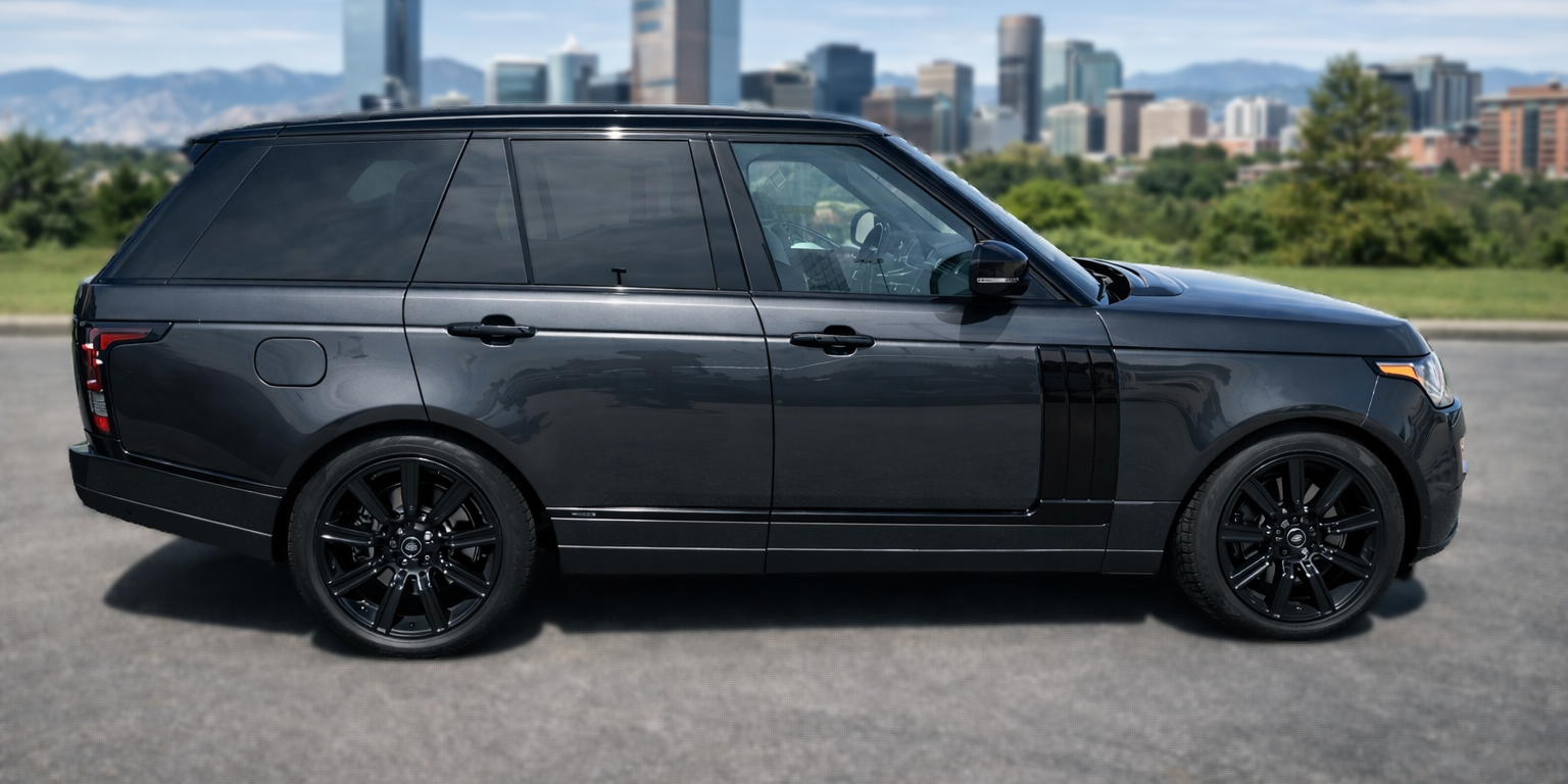 Dark gray Range Rover SUV with black wheels driving in front of a city skyline.