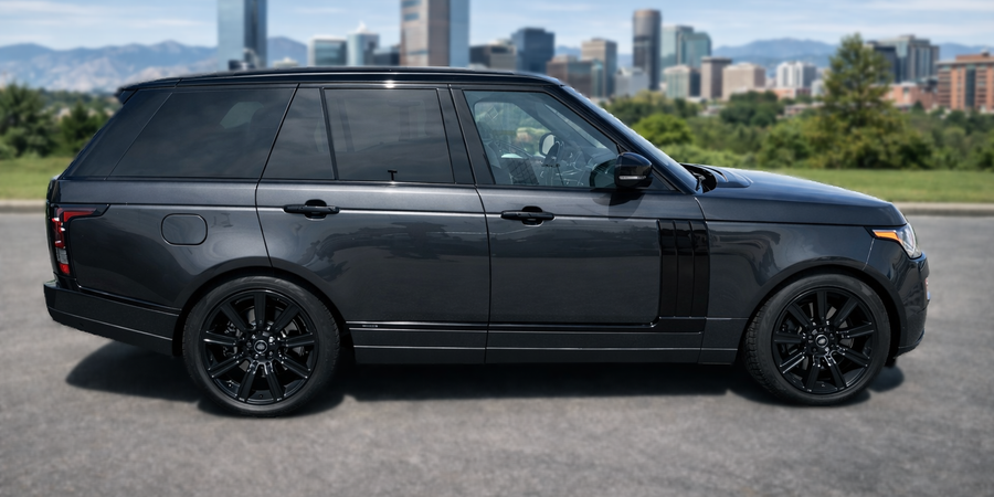 Dark gray Range Rover SUV with black wheels driving in front of a city skyline.