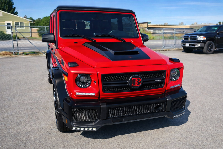 Red and black Brabus G-Wagon SUV parked outside. Front view, showing custom grill, hood scoop, and black accents.