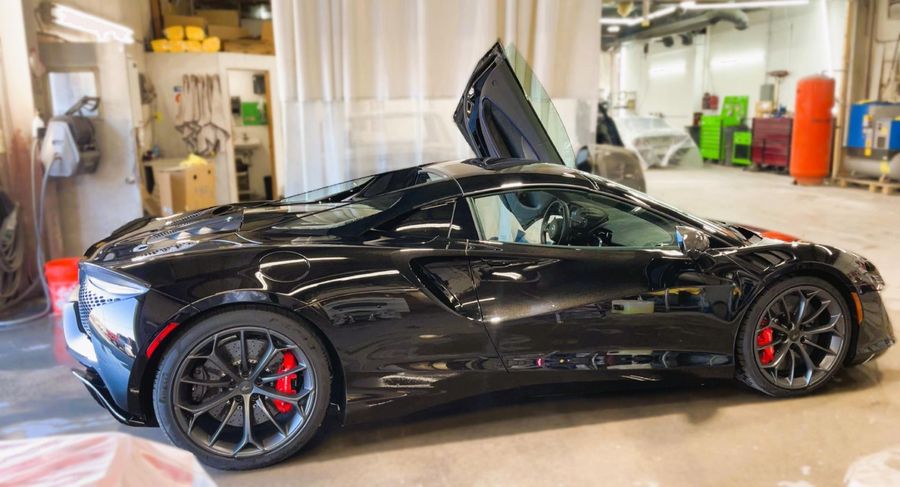 Black sports car with butterfly doors open in a workshop. Red brake calipers visible.