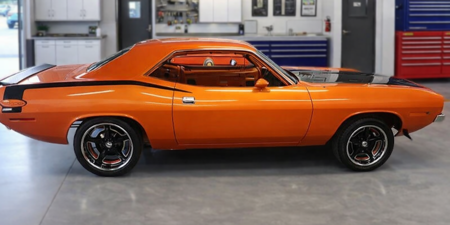 Orange vintage car parked indoors with black racing stripes.