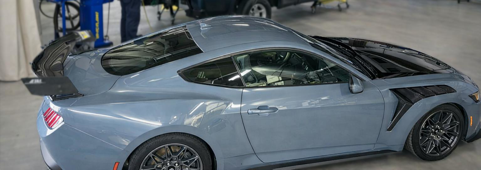 A gray sports car with black accents and a large spoiler parked in a garage.
