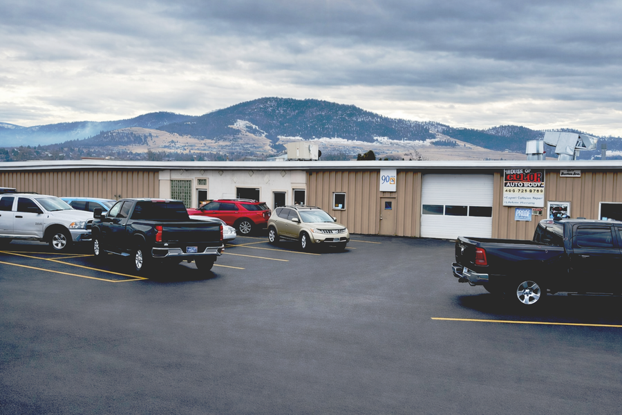 Cars parked in front of a tan building, House of Color Auto Body, mountains in the background under a cloudy sky.