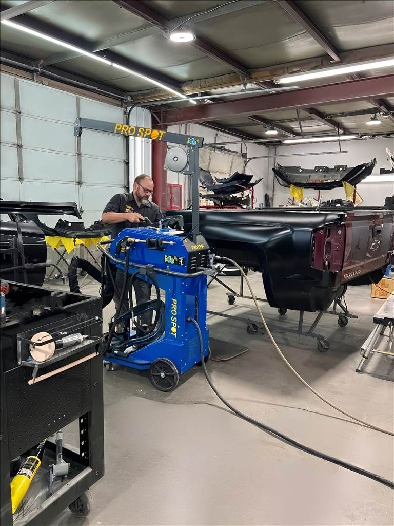 Man working on a car in a body shop, using a blue welding machine in House of Color Auto body and paint shop.