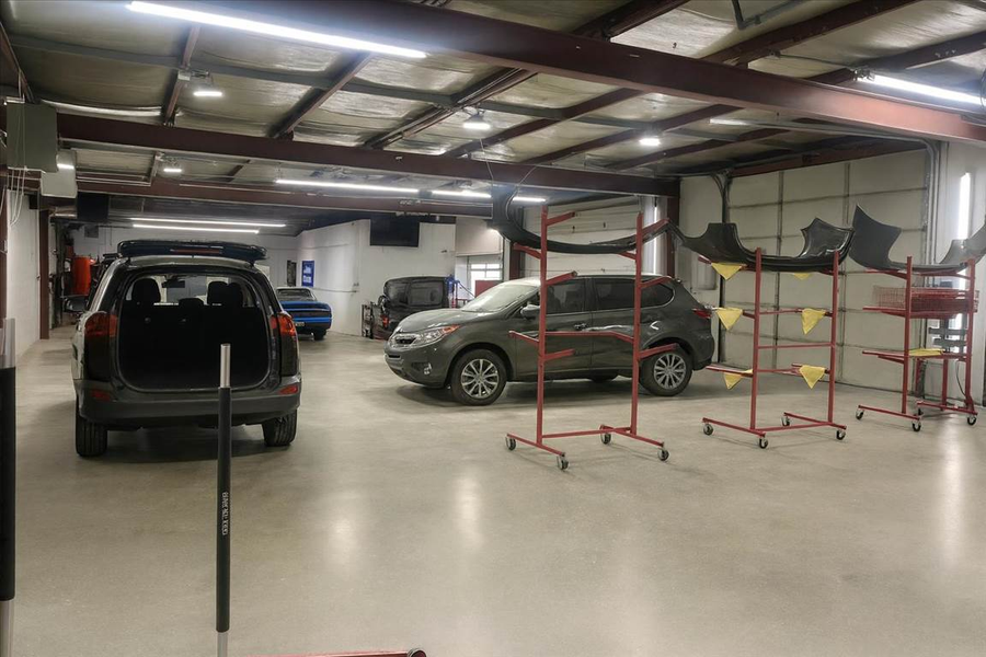 Inside a car repair shop, House of Color several vehicles parked. Equipment stands in the foreground; bright lighting.
