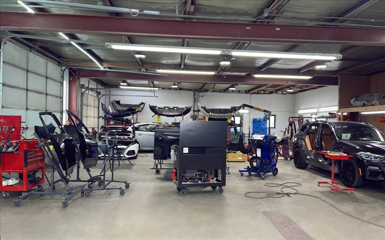 Inside a car body shop, House of Color; vehicles, tools, and equipment are arranged, with garage bay door open.