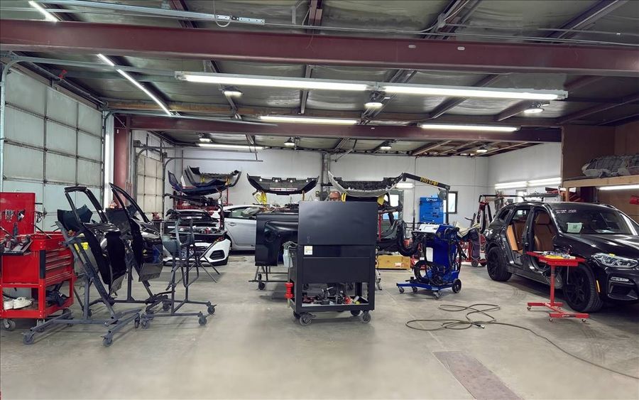 Inside a car body shop, House of Color; vehicles, tools, and equipment are arranged, with garage bay door open.