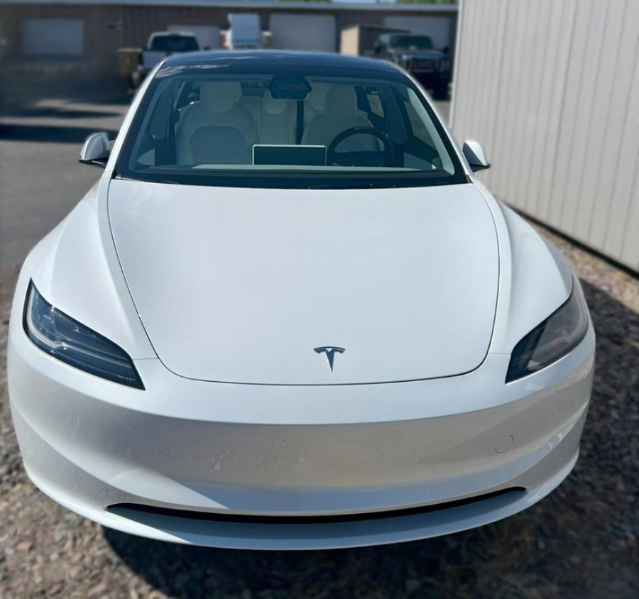 White Tesla car, front view, black roof, parked outside.