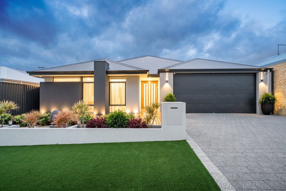A Modern House With a Black Garage Door and a Lush Green Lawn — Goulburn Roofing In Goulburn, NSW