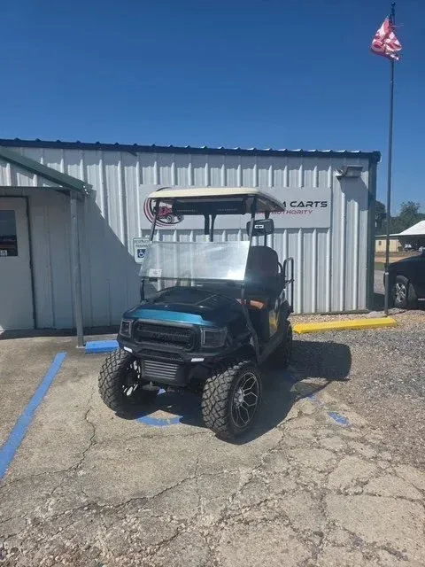 Blue and black golf cart with large tires parked in front of a building with 