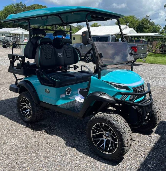 Teal golf cart with black accents, off-road tires, and canopy, parked outdoors.