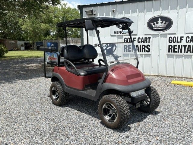 Maroon golf cart parked on gravel outside a golf cart rental building