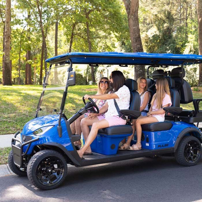 Three modern golf carts in red, blue, and silver parked in a row outside a white building under a clear blue sky.