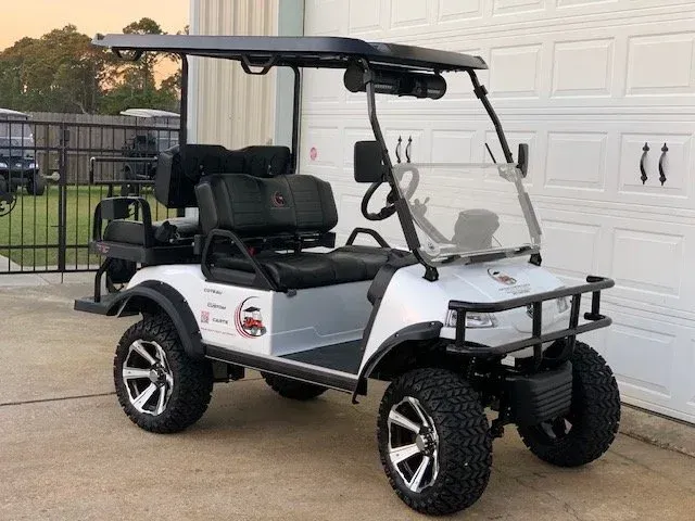 White golf cart with black roof, off-road tires, and front bumper parked near a white garage door.