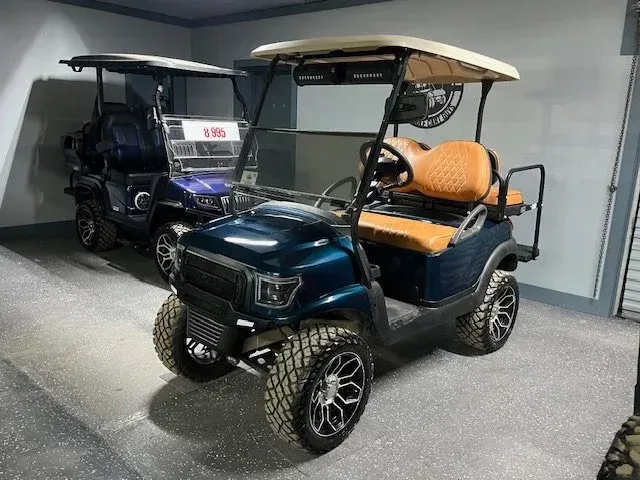 Two teal golf carts with tan roofs and seats parked indoors.