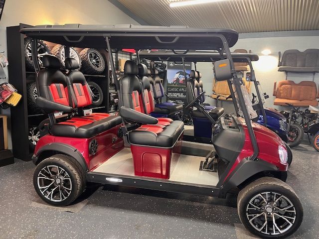 A red and black four-passenger golf cart with custom alloy wheels parked inside a showroom with various parts.