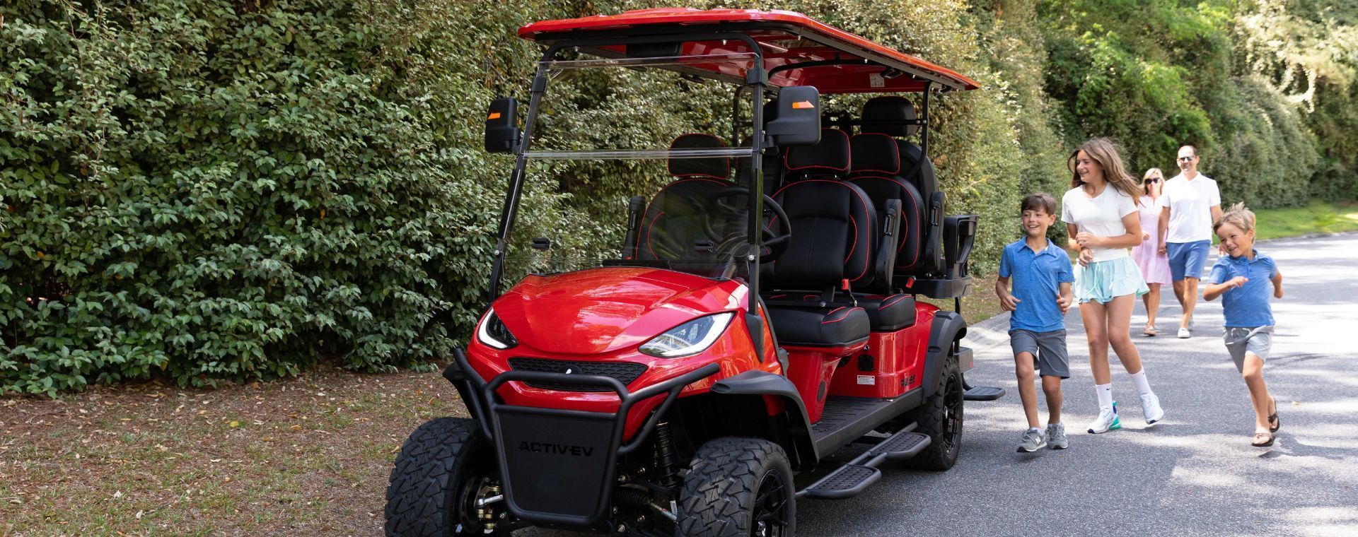 A black Solana electric cart parked on a dirt path by a wooden barn, with three people standing and talking nearby.