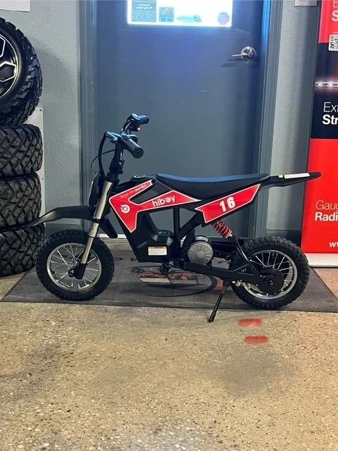 Black and red electric dirt bike parked on a cement floor near a stack of tires and a door.