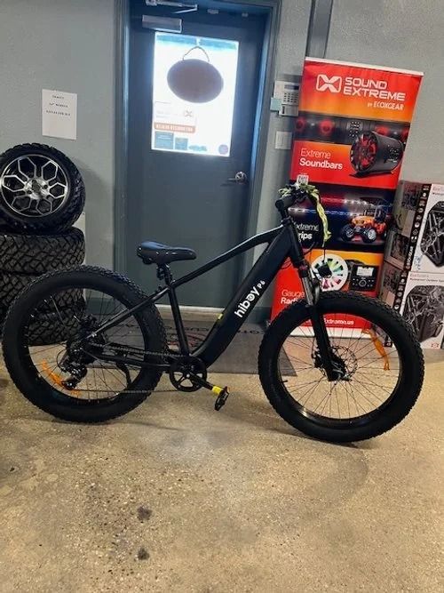 Black fat tire electric bike in a shop with a Sound Extreme banner.