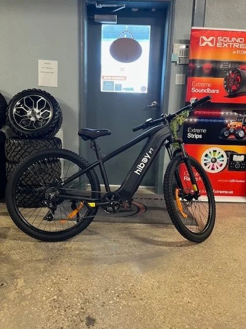 Black electric bike in a shop setting, next to a door and stacked tires.