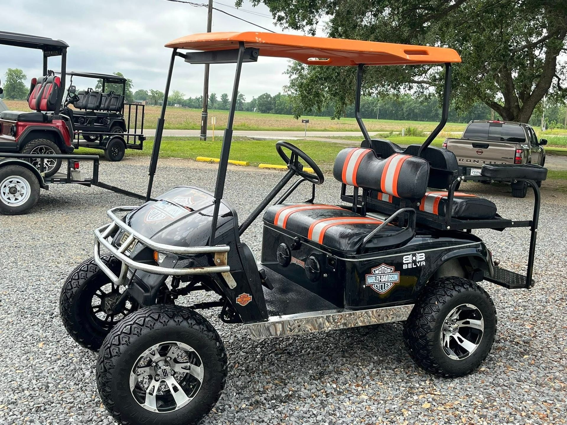 Black and orange custom golf cart with large tires, parked on gravel.