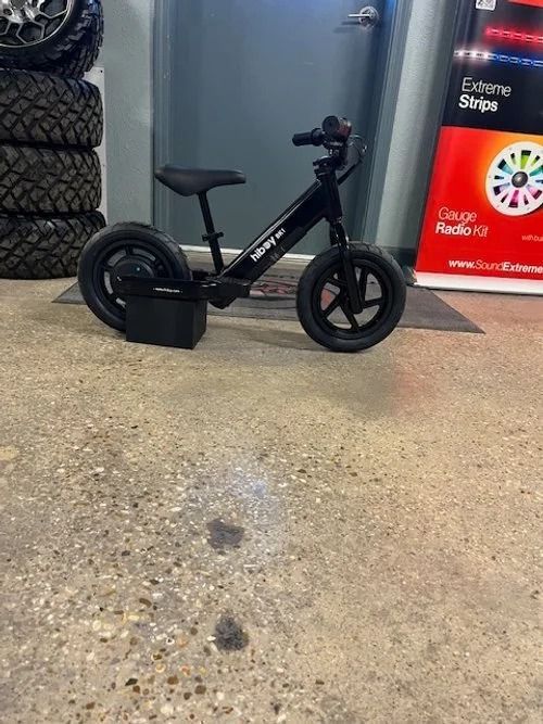 Black balance bike with black tires and seat, parked indoors.