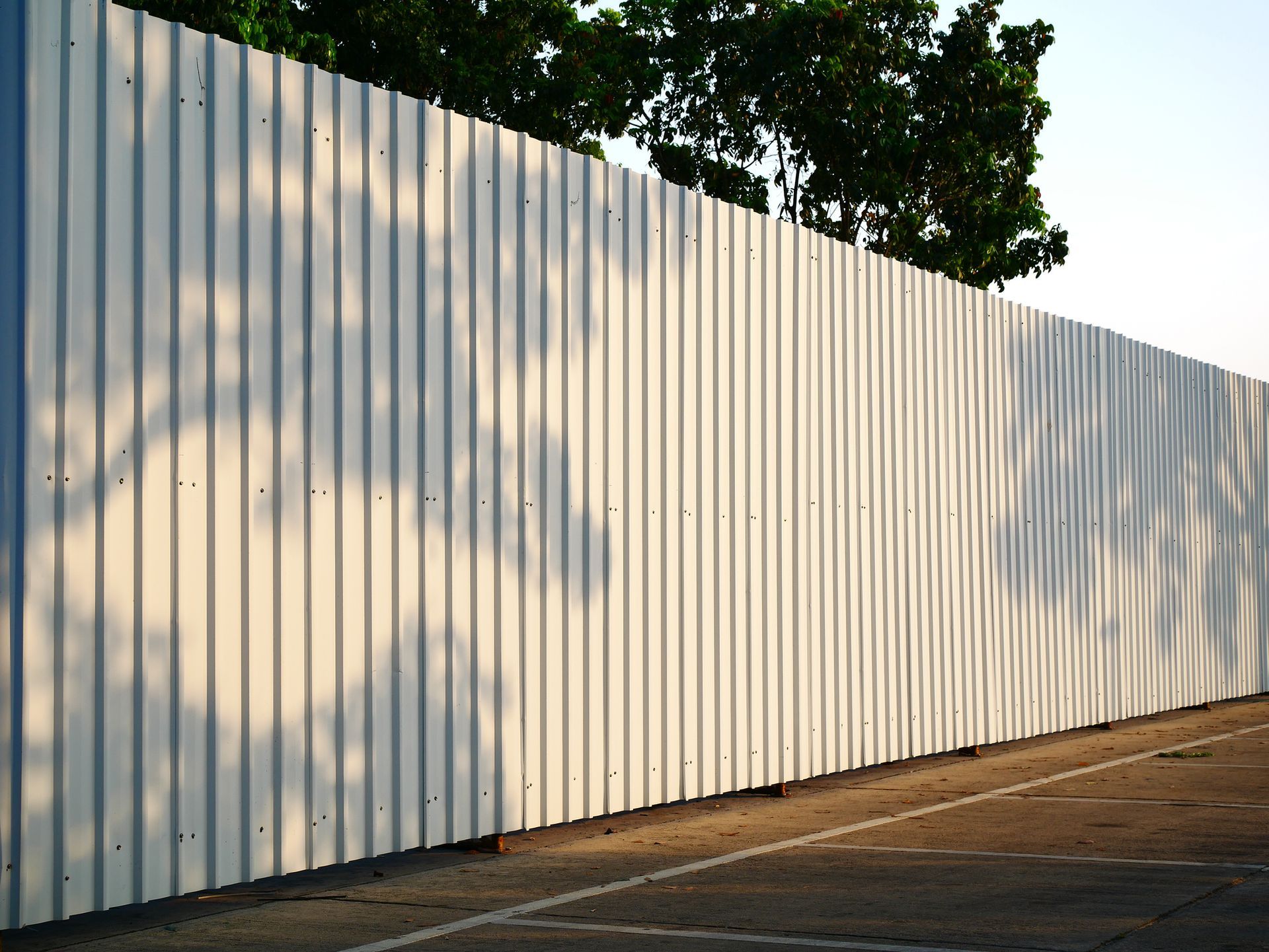 A white fence is surrounding a parking lot with trees in the background
