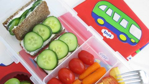 A lunch box filled with sandwiches , cucumbers , tomatoes and carrots.