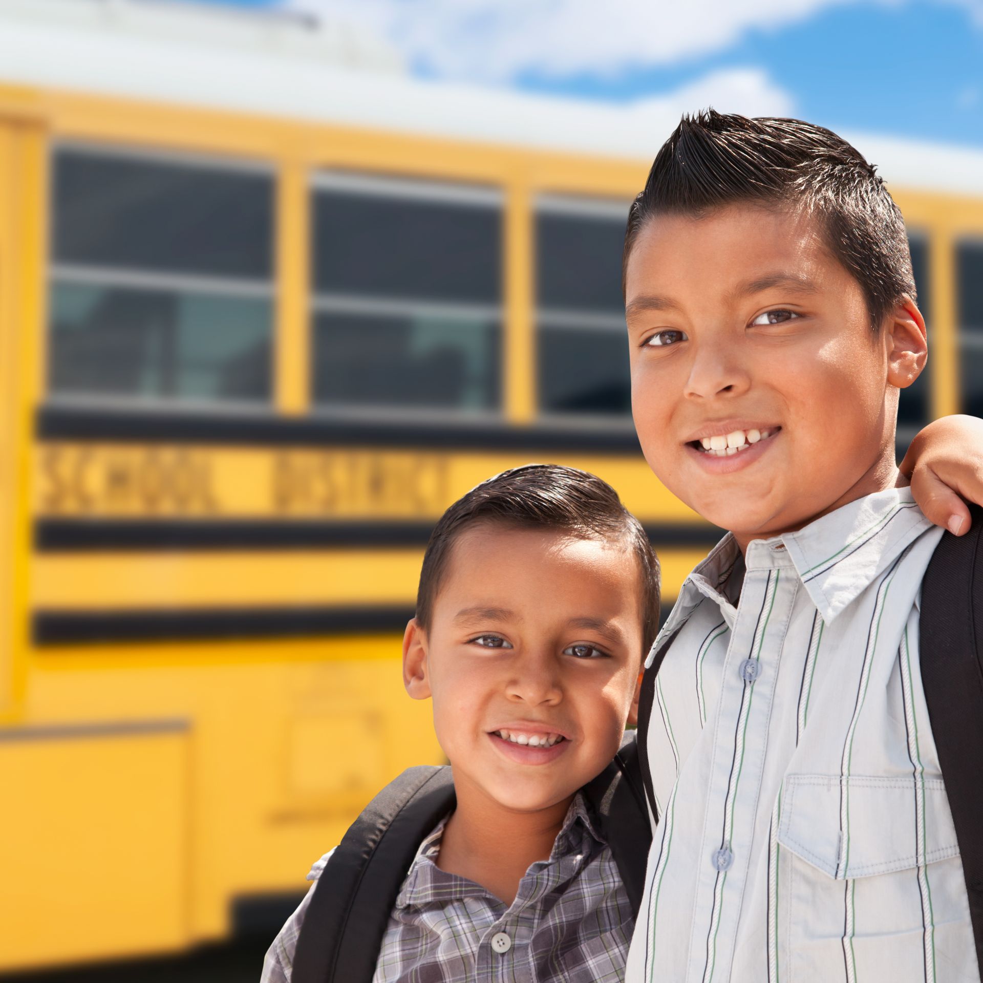 Two young boys pose in front of a yellow school bus