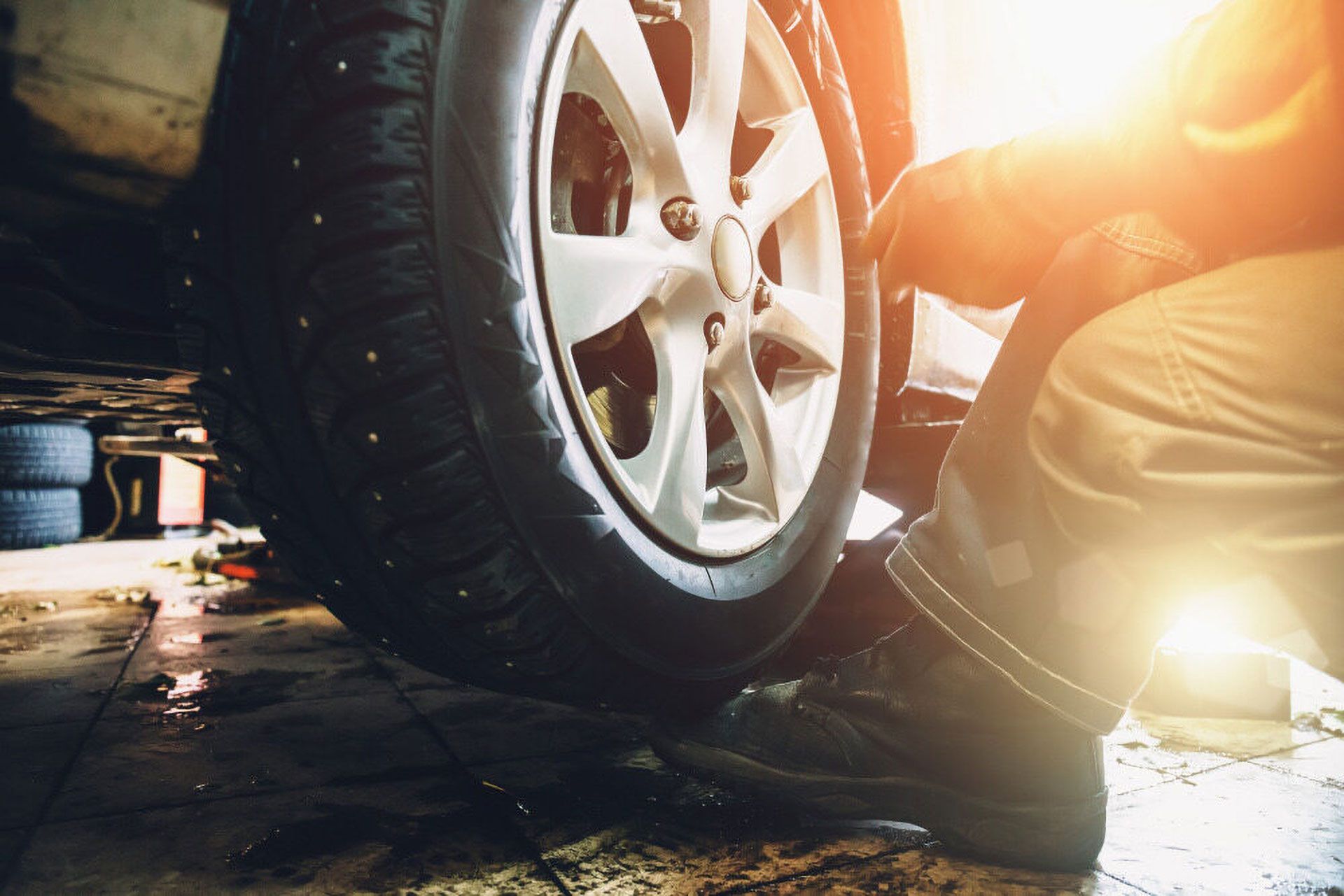 A mechanic working on a car wheel inside a brightly lit automotive repair shop.