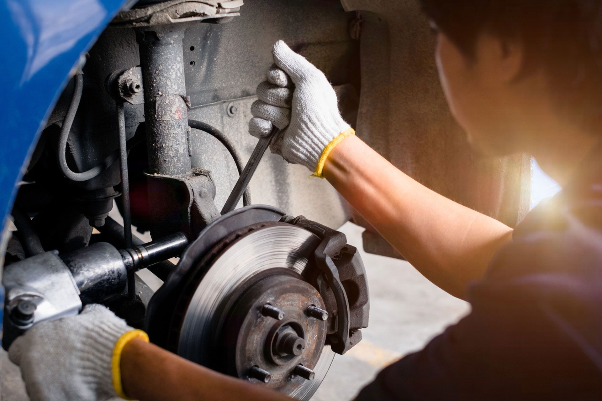 A mechanic in work gloves uses power and hand tools to repair the brake system of a car in a garage.