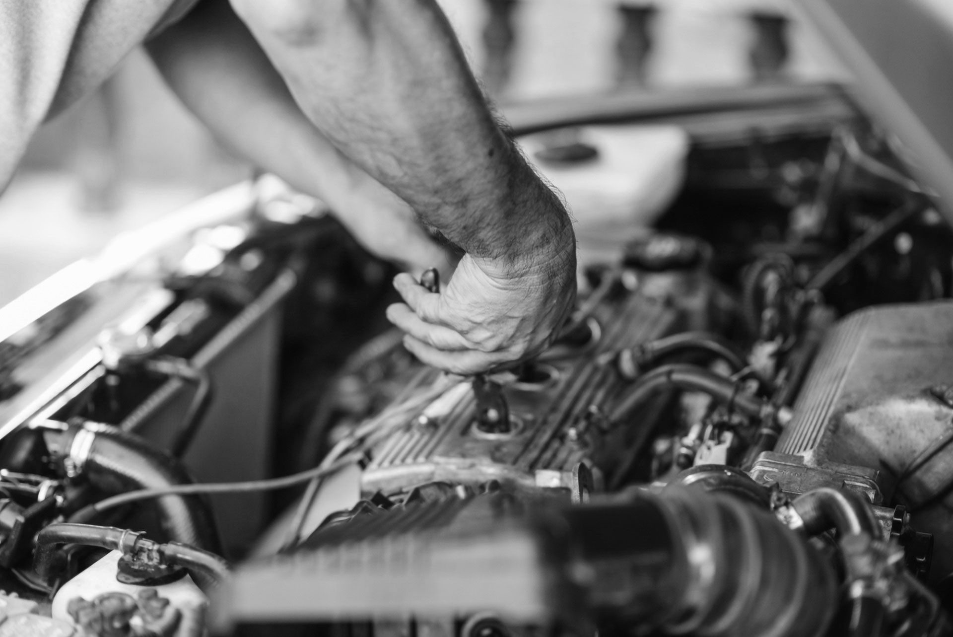 A person works on a car engine, holding a tool and adjusting blue cables connected to the engine block.