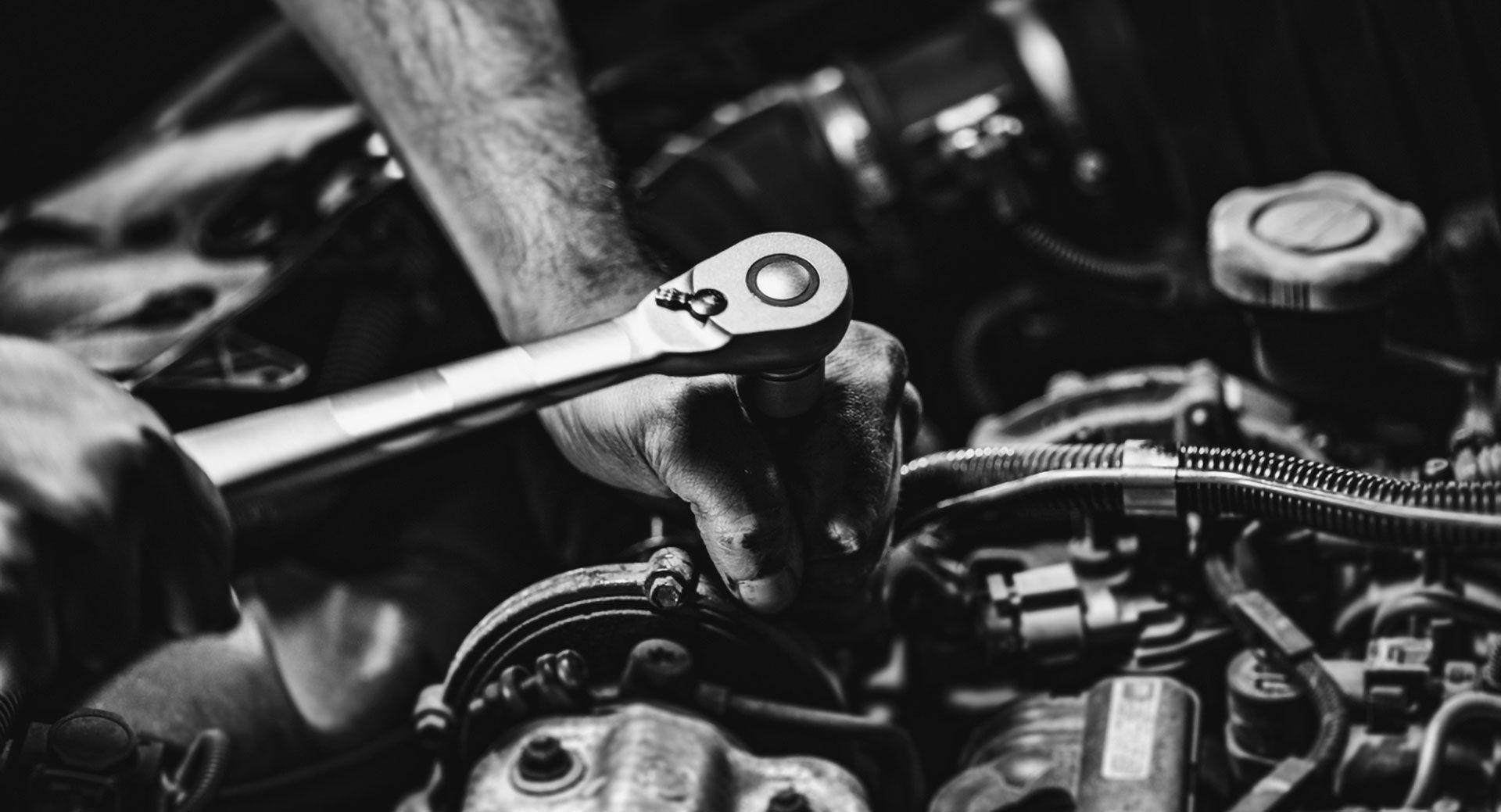 A mechanic's hands use a ratchet to tighten a bolt on a car engine.
