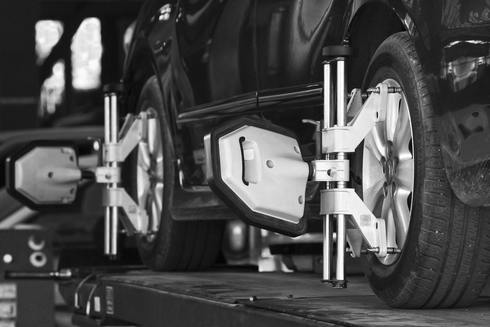 A car undergoing a wheel alignment service at a repair shop, with reflective sensors attached to its wheels.