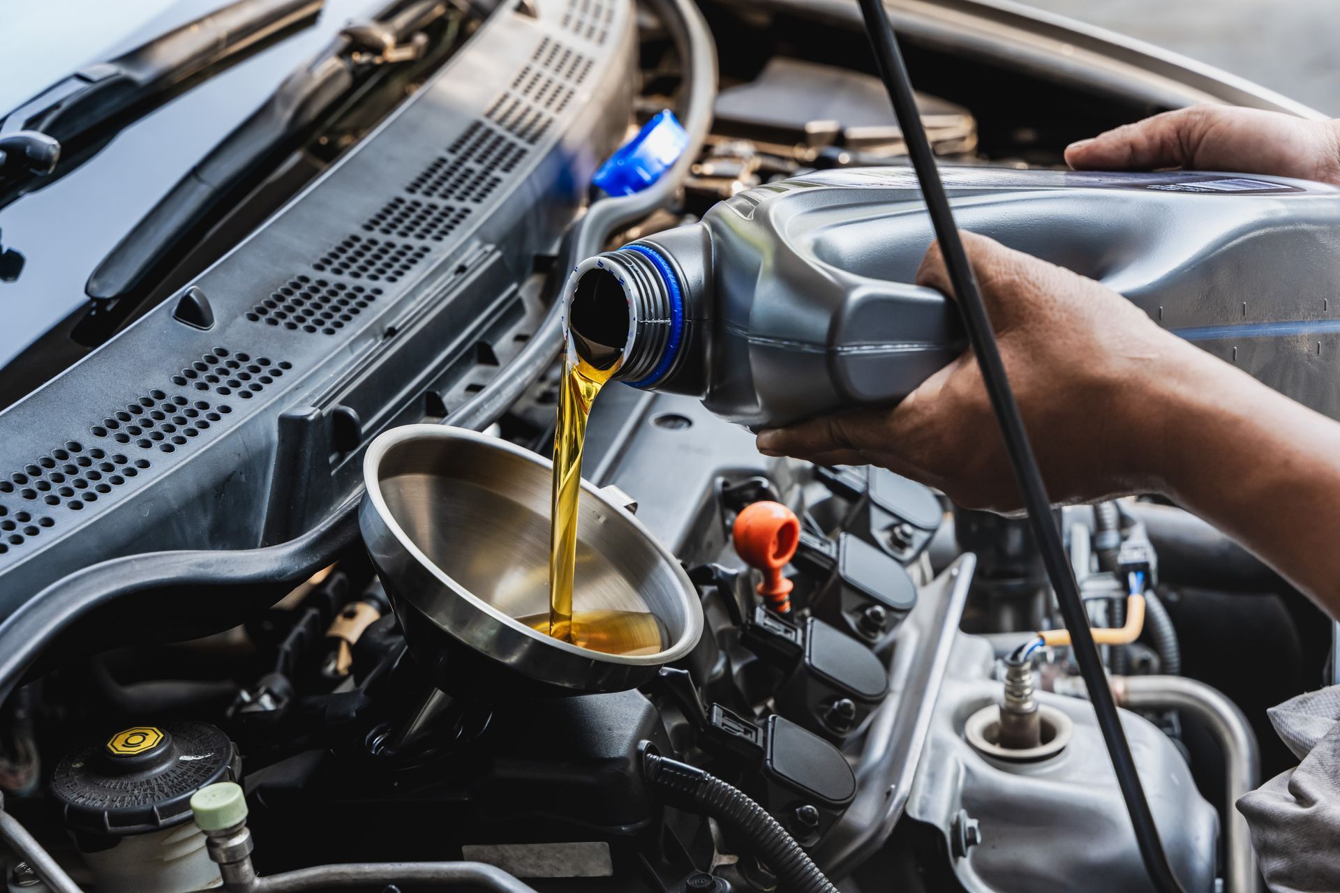 A person pouring golden engine oil from a plastic jug through a funnel into a car engine.