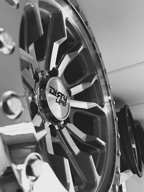 A black and white close-up shows a large, stylized aftermarket vehicle wheel with the