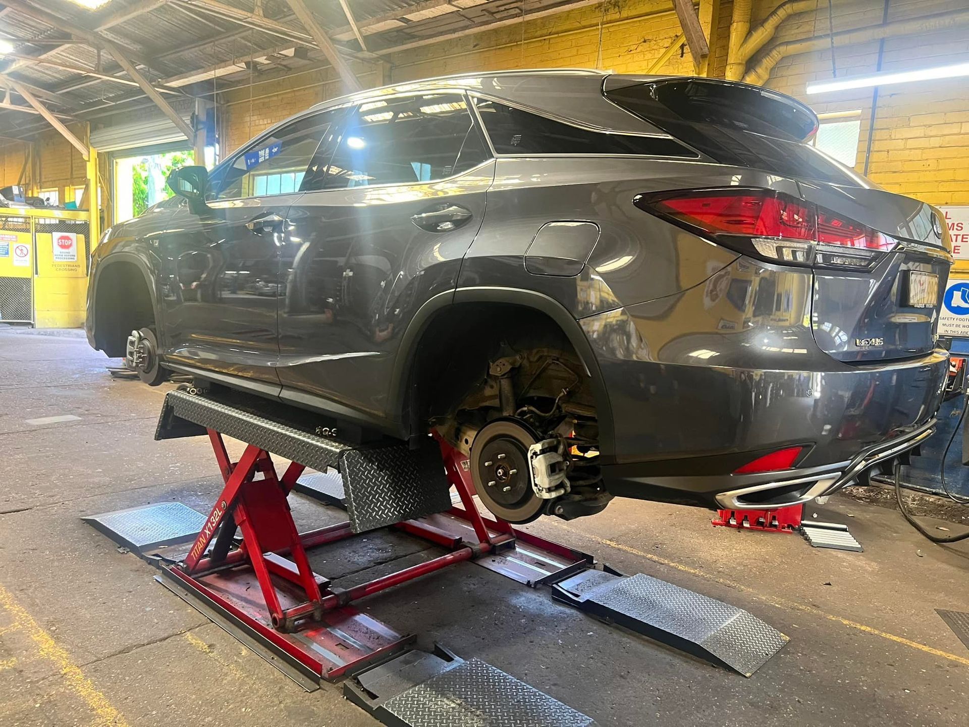 A gray SUV elevated on a red hydraulic scissor lift inside an auto repair shop with its rear wheel removed.