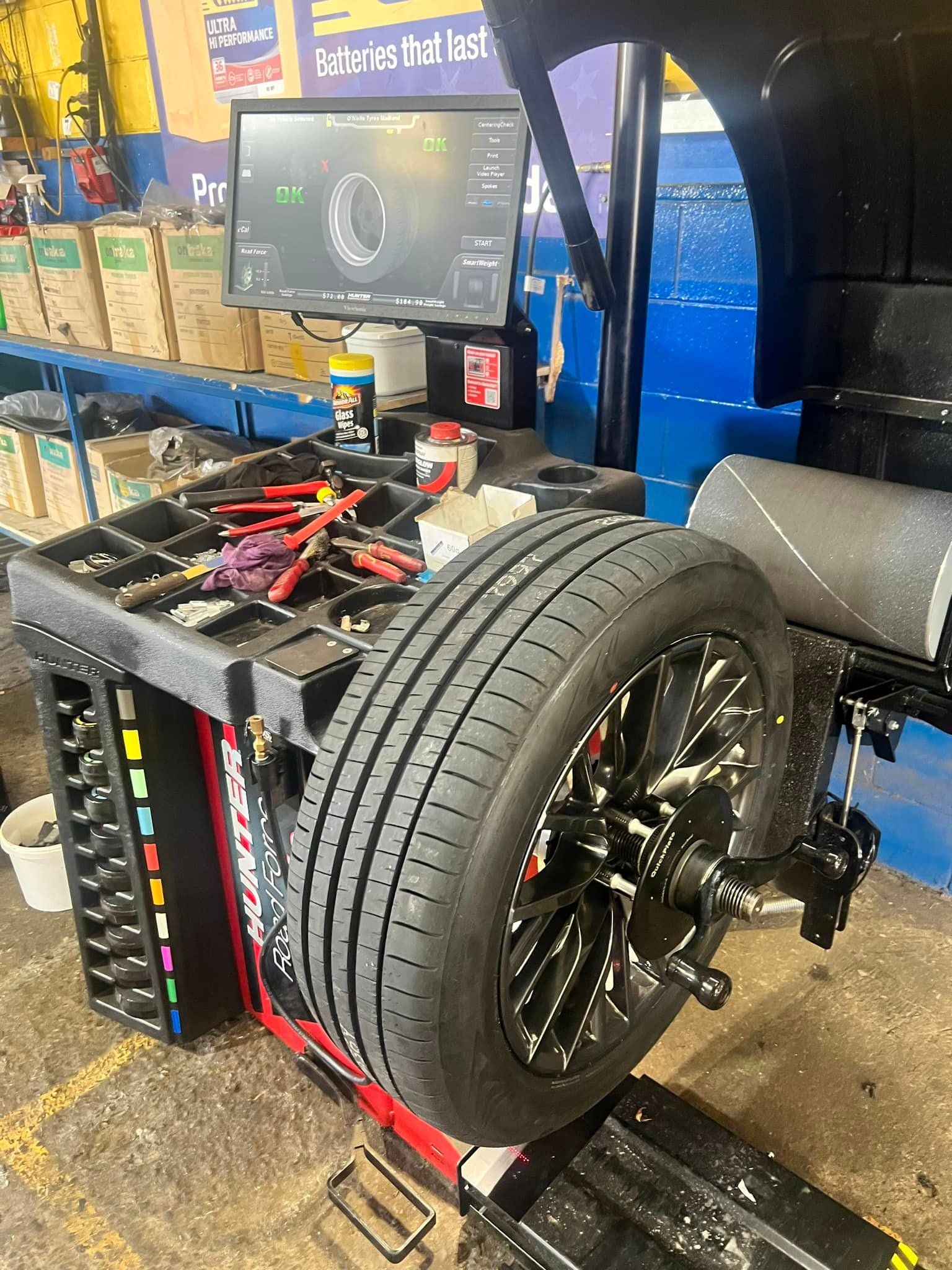 A car tire mounted on a Hunter wheel balancing machine in an auto repair shop with tools on a tray nearby.