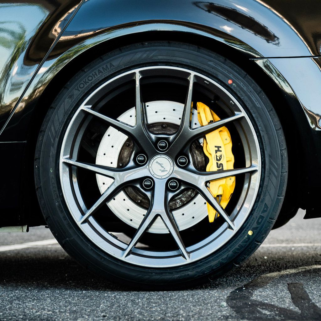 Close-up of a black car's wheel with a grey multi-spoke rim, yellow brake caliper, and Yokohama tire on asphalt.