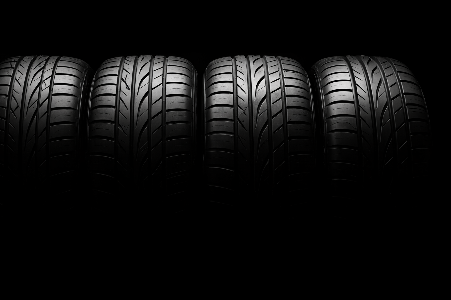 Four black tires with detailed tread patterns lined up against a dark, minimalist background.