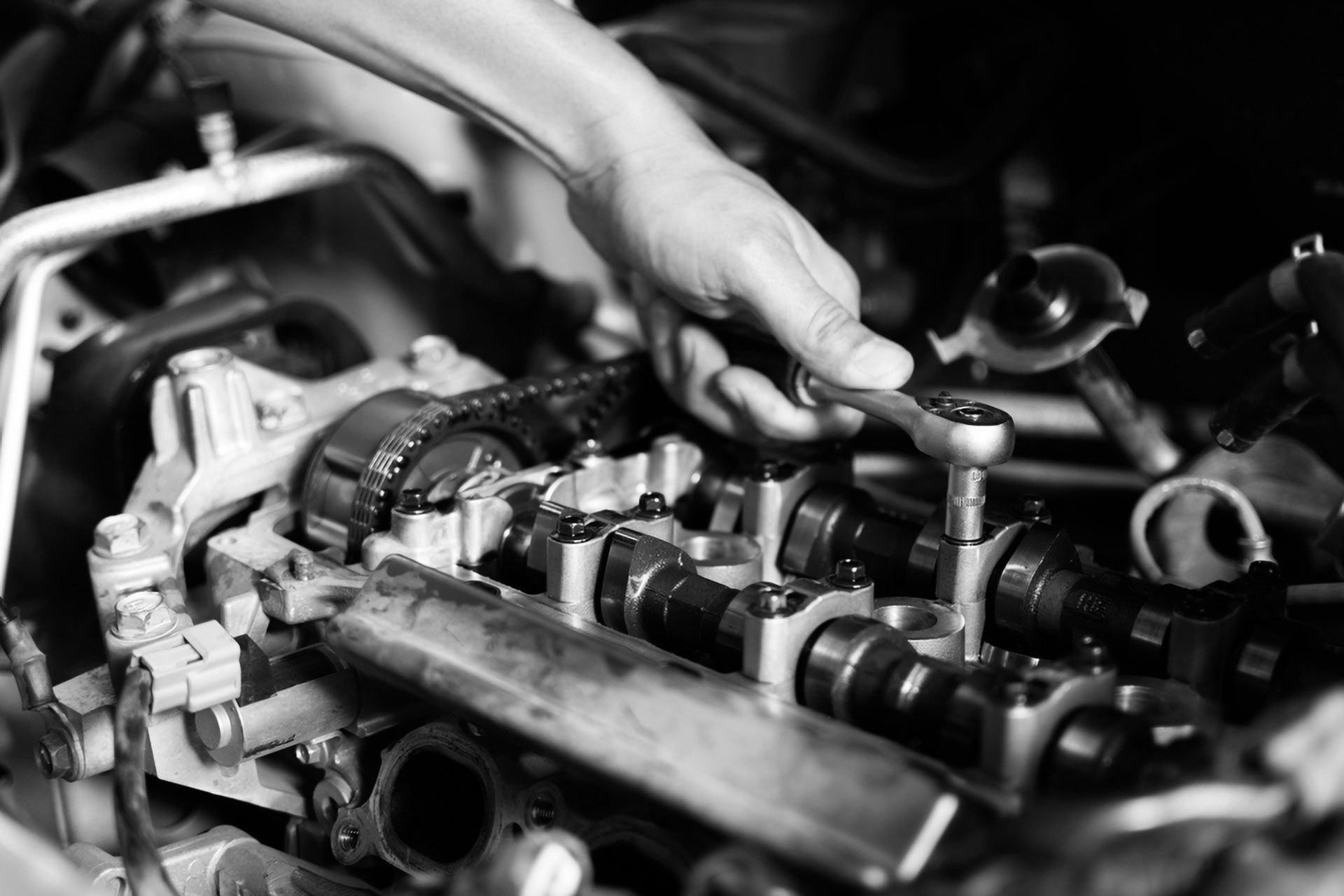A person uses a ratchet wrench to work on a car engine with visible camshafts.