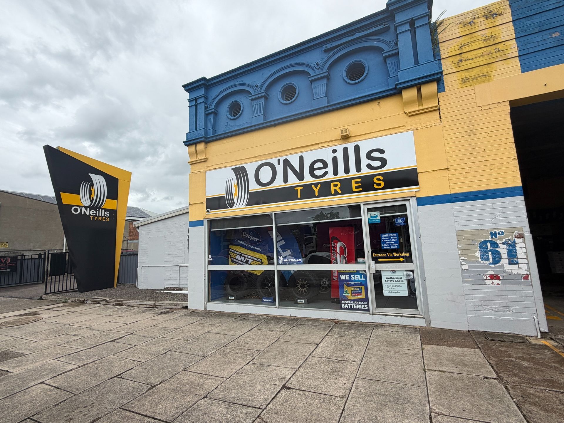 O'Neills Tyres shop front with a blue and yellow facade, a covered service entrance, and parked cars in the lot.