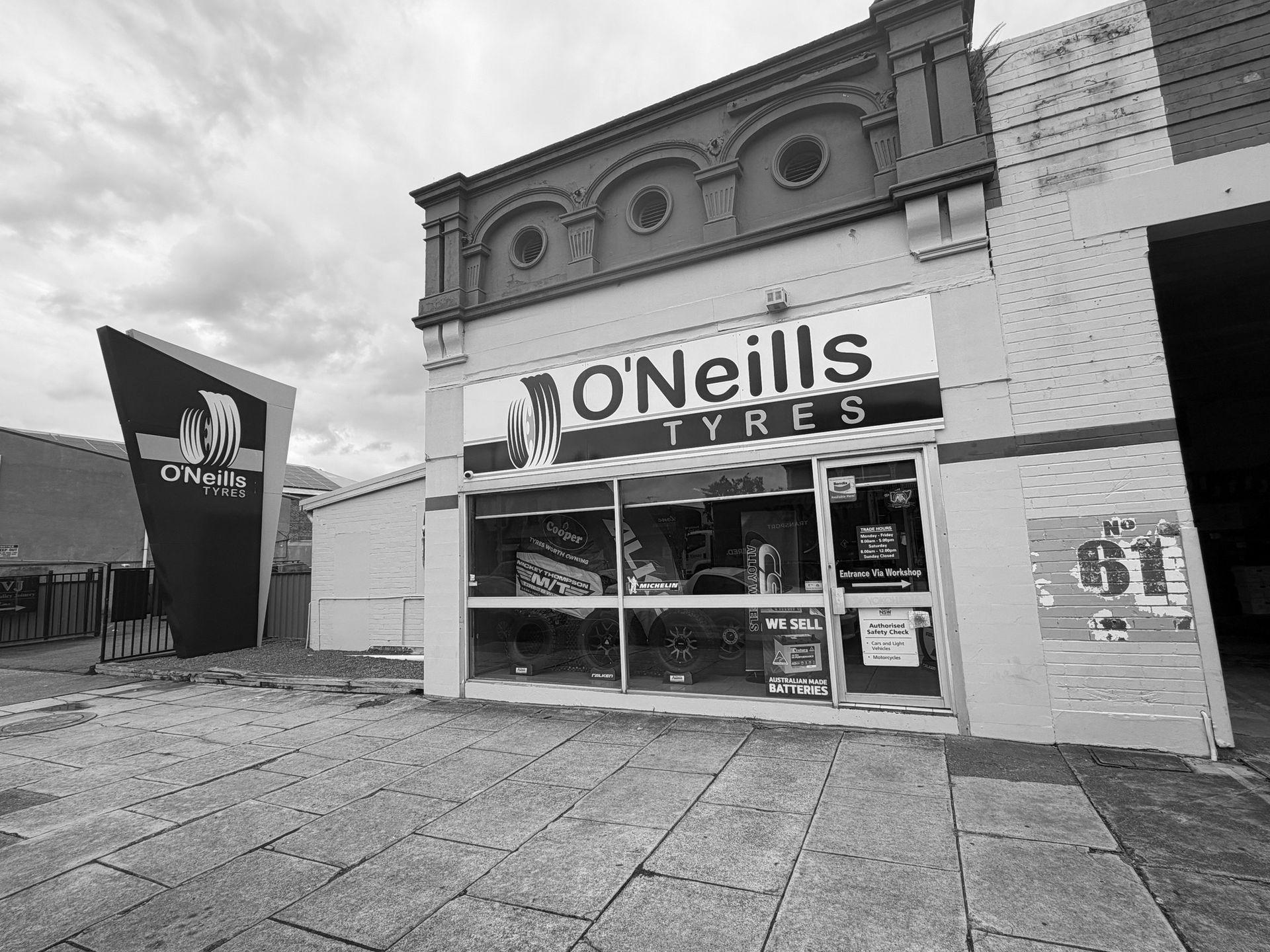 O'Neills Tyres storefront with a yellow facade, blue trim, and a black promotional sign on a cloudy day.