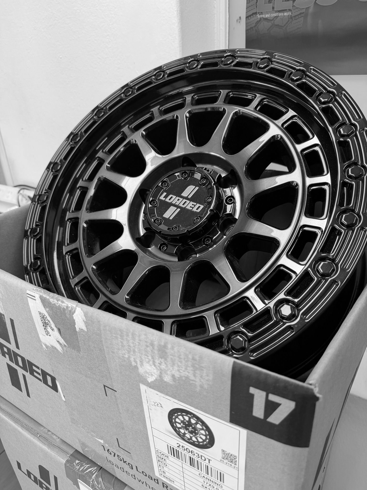 A glossy black 17-inch off-road wheel with a multi-spoke design and simulated beadlock rim, resting in a cardboard box.