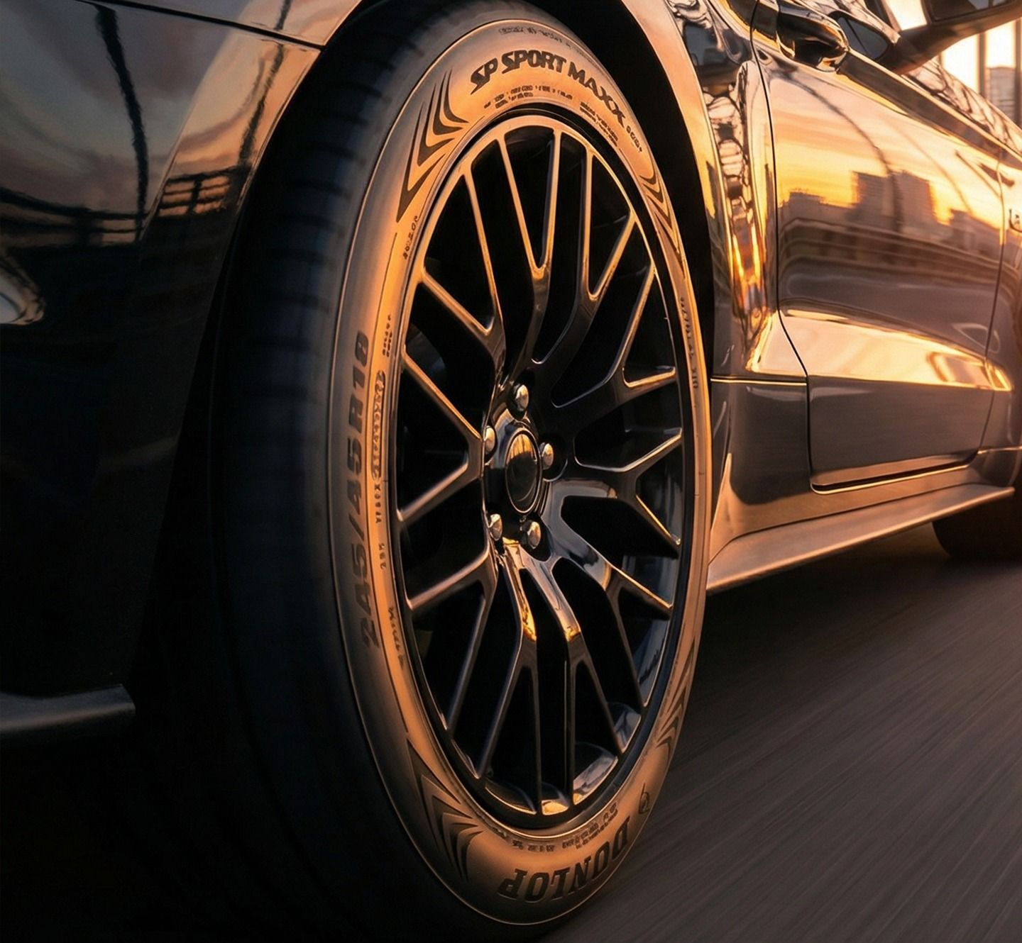 Close-up of a sleek black car wheel and tire against a warm, glowing sunset backdrop.