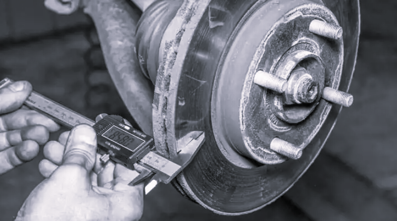 A mechanic uses a digital caliper to measure the thickness of a vehicle's metal brake rotor.