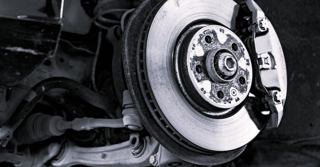 A close-up view of an automobile disc brake assembly, showing the brake rotor, caliper, and suspension components.
