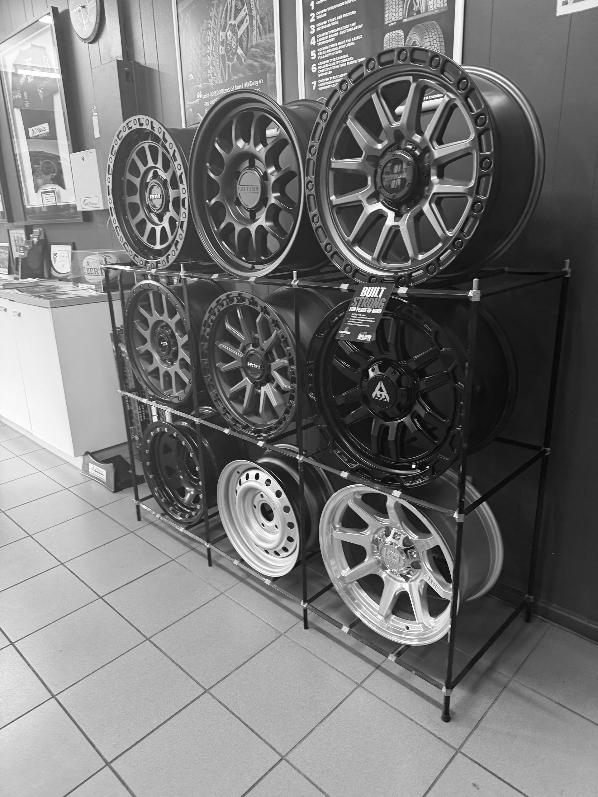 A display rack in a shop featuring various black, silver, and metallic aftermarket car wheel rims.