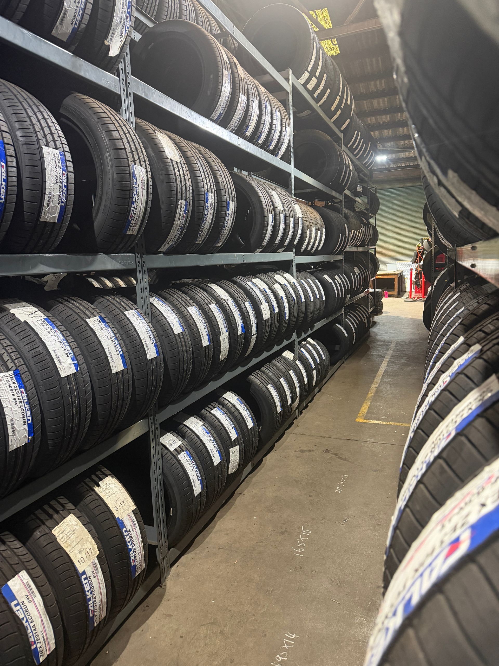 Rows of black tires stacked on metal industrial shelving units in a warehouse.