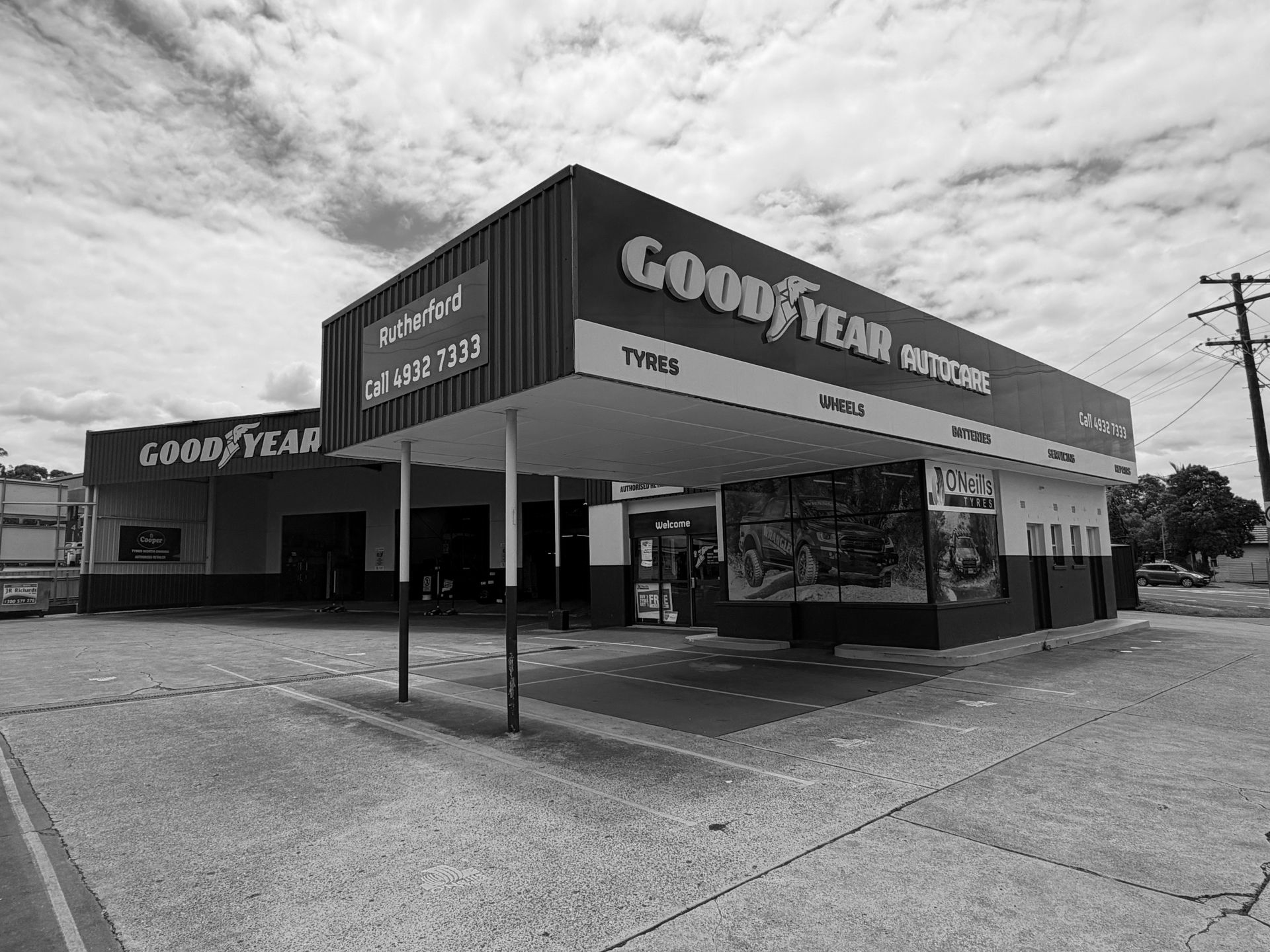 A Goodyear AutoCare service center with a blue and yellow exterior, featuring a large canopy over a paved parking area.
